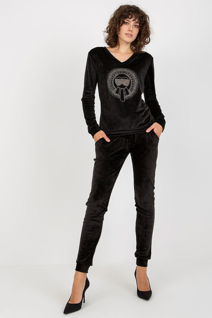 Model in a black luxury velour blouse and pants set with a heart neckline by Relevance, combining elegance with comfort and stylish black heels.