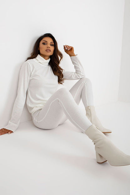 A stylish model seated, wearing elegant white striped leggings paired with a matching high-neck top, showcasing everyday luxury. Featured by Lakerta, the leggings provide a high waist design for a refined silhouette.