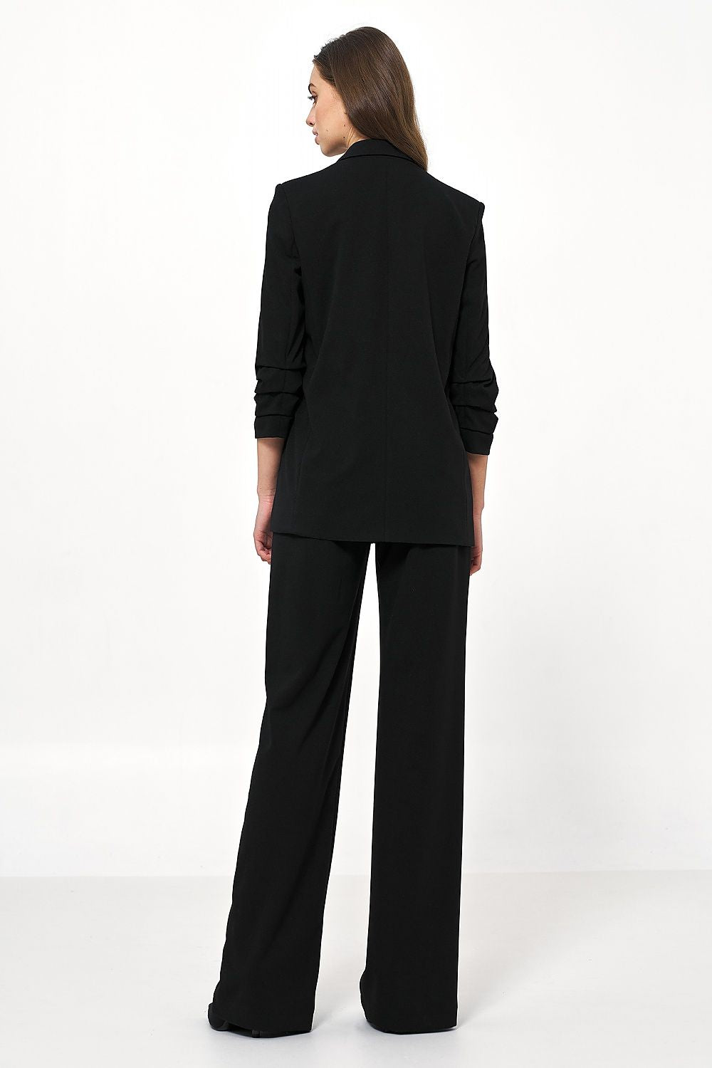 Back view of a luxurious black Nife women's jacket with creased sleeves, highlighting its contemporary design when styled with tailored trousers.
