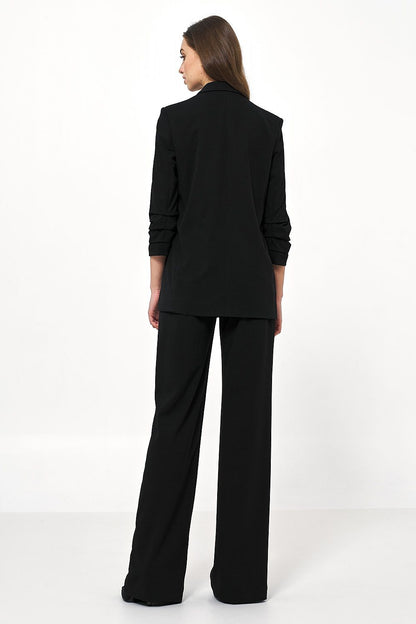 Back view of a luxurious black Nife women's jacket with creased sleeves, highlighting its contemporary design when styled with tailored trousers.