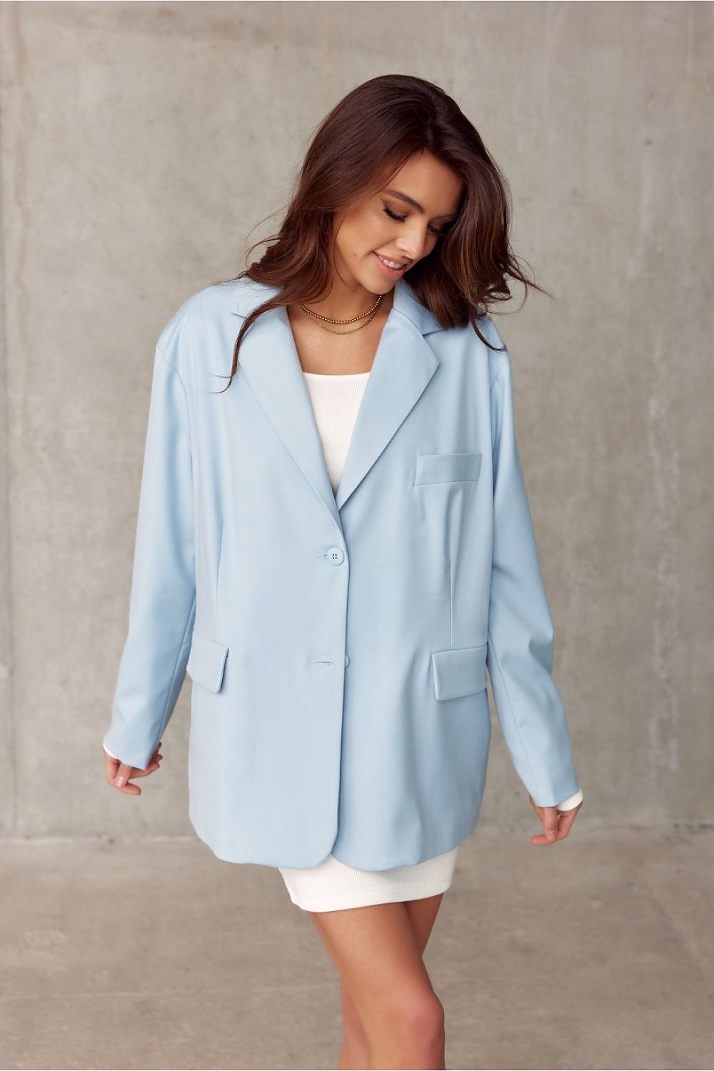 Roco Fashion voluminous cut light blue jacket with elegant buttons and imitation pockets, styled elegantly over a white dress against a textured grey background.