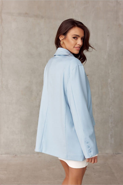 Elegant voluminous cut jacket by Roco Fashion, featuring soft blue fabric, a classic collar, and sophisticated button details. The model showcases the jacket with a delicate pose against a minimalist background, highlighting its formal and stylish appeal.