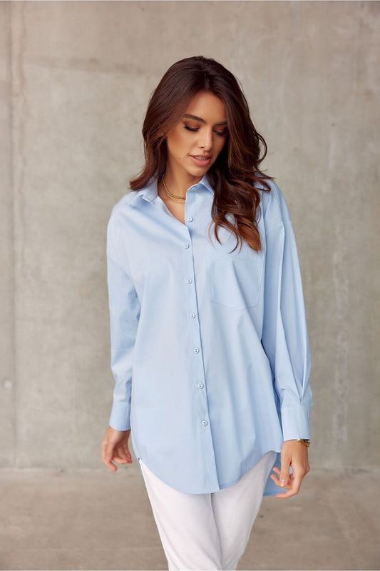 Elegant blue oversized long sleeve shirt by Roco Fashion, featuring a classic collar and asymmetrical hem, styled with white trousers for a modern chic look.