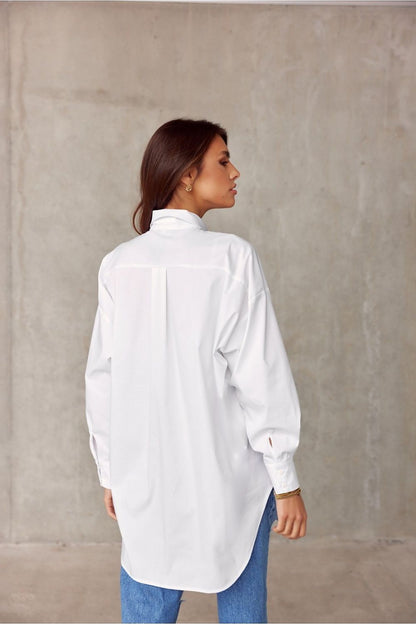 Elegant Roco Fashion women's oversized long sleeve shirt, featuring an asymmetrical hem, displayed from the back against a minimalist concrete backdrop.