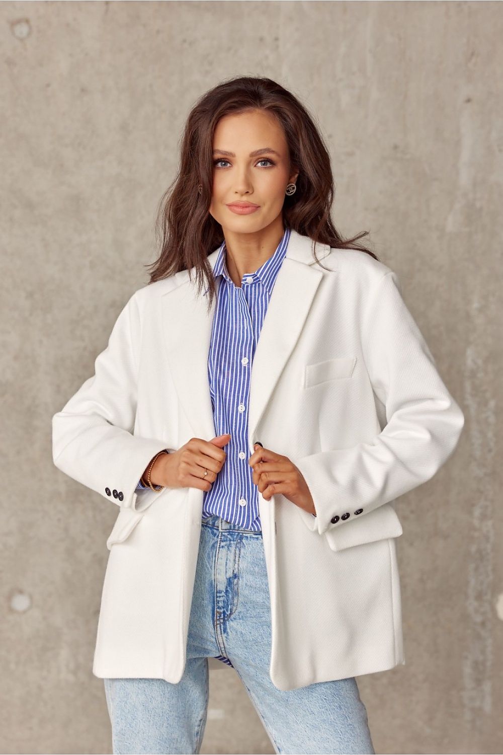 Close-up of a model in a fashionable white voluminous jacket from Roco Fashion, elegantly posed with a blue striped shirt and light denim, showcasing a blend of sophistication and casual elegance.