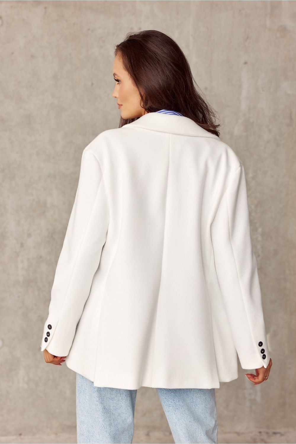 Back angle view of a model wearing a pristine white Roco Fashion voluminous jacket, paired with a blue striped top and denim, emphasizing the stylish design and luxurious fabric in an urban environment.