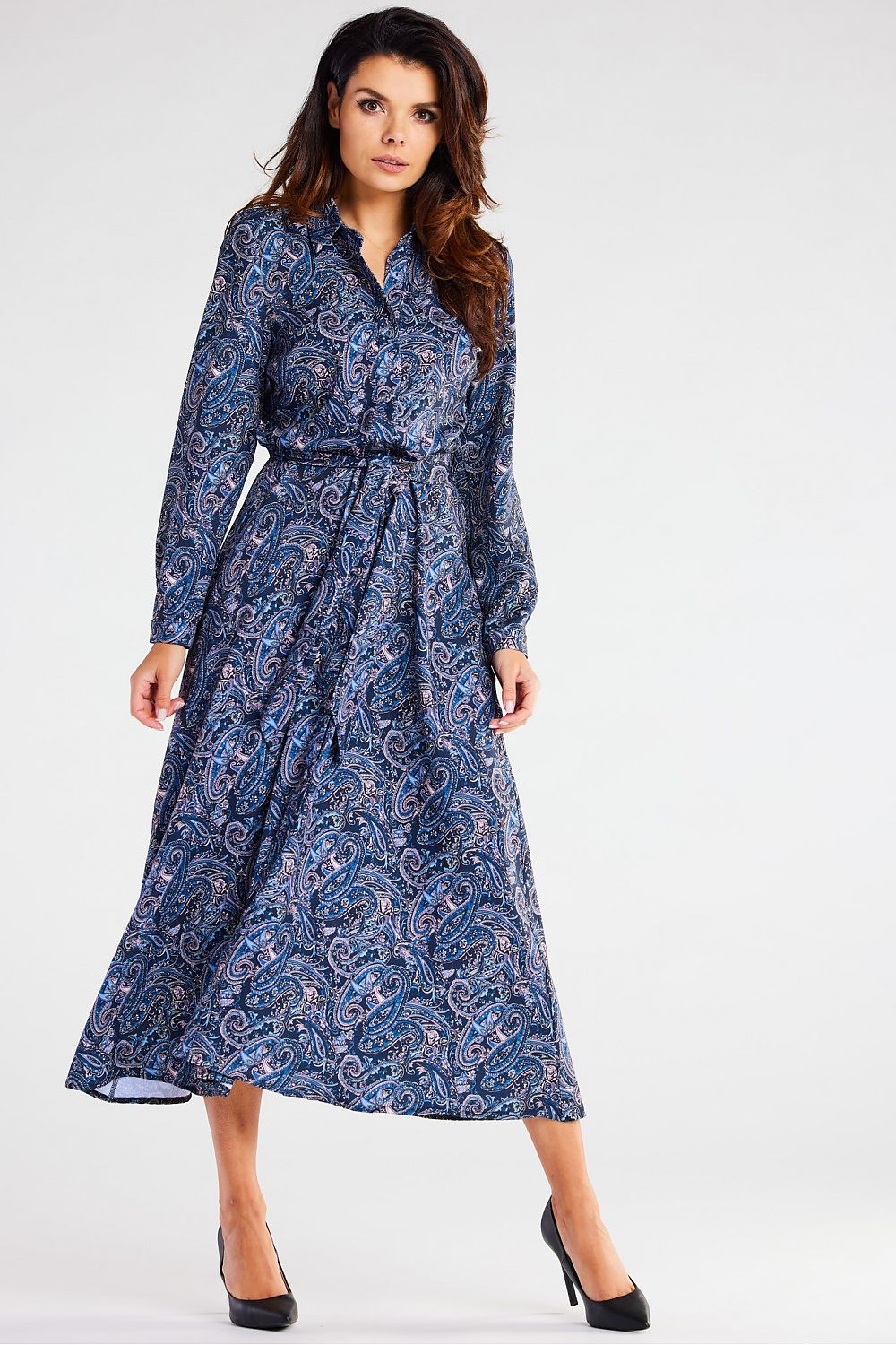 Sophisticated model showcasing an elegant Awama maxi dress with a flared hem and long sleeves, styled with heels, in a luxurious setting.