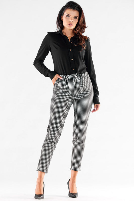 Elegant woman's casual trousers by Awama, featuring a chic black and white houndstooth pattern, designed with an elastic waist and pockets, paired with a stylish black button-up shirt.