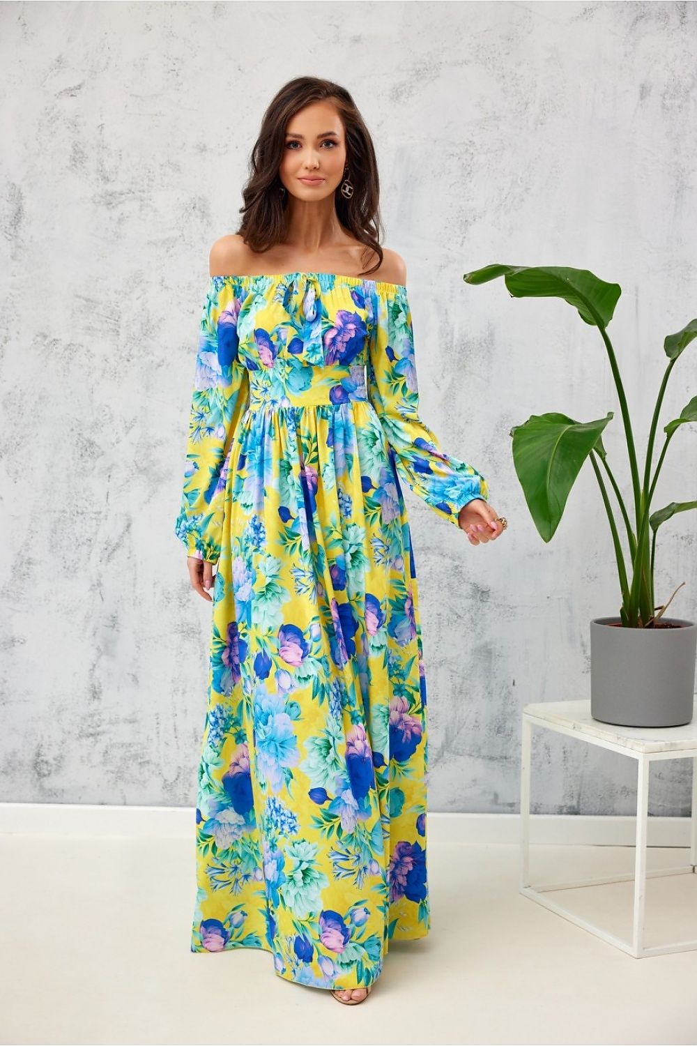 Elegant long Spanish maxi dress by Roco Fashion featuring an open shoulder design, vibrant floral pattern in yellow and blue, perfect for an evening occasion.