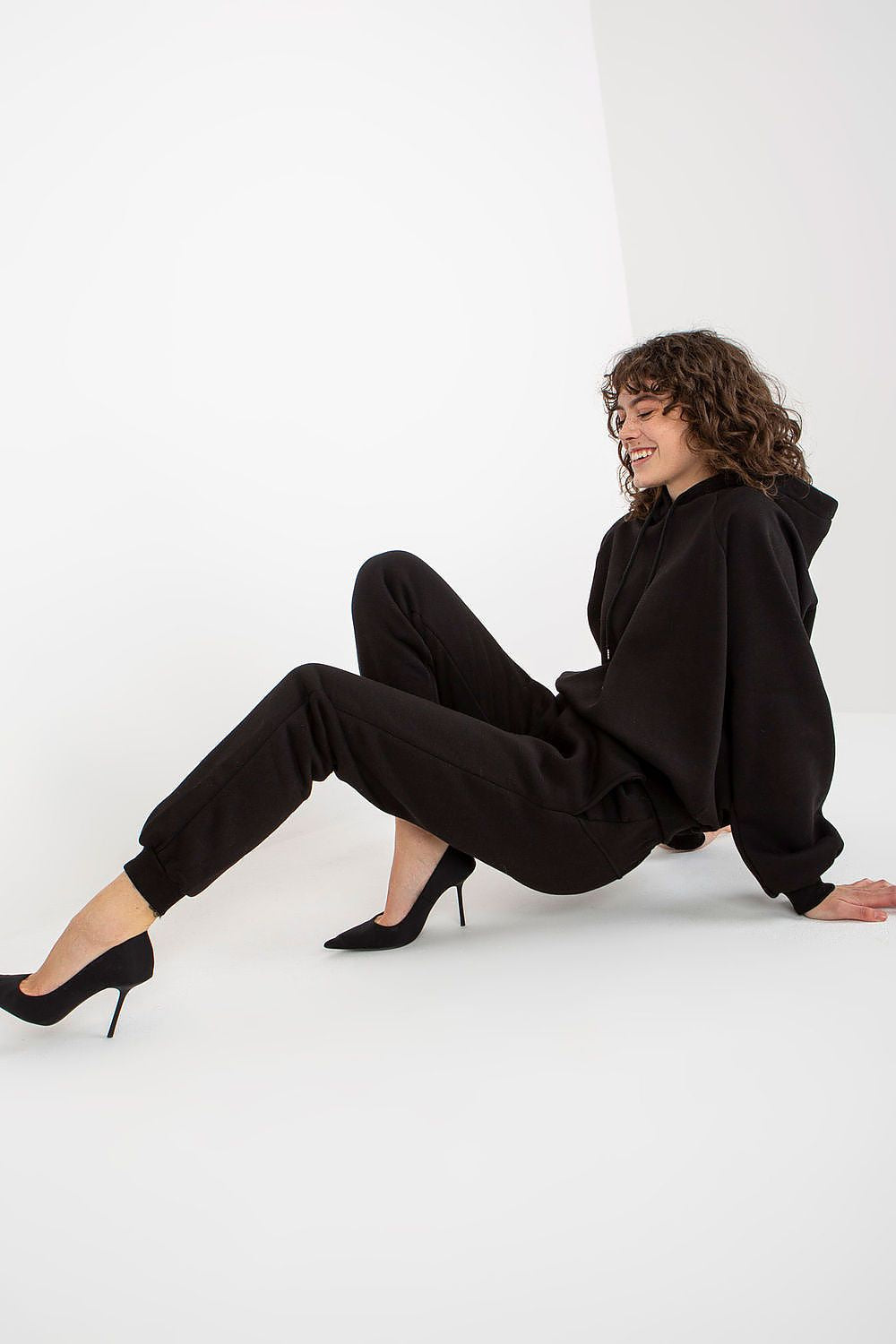 Ex Moda luxurious black sweatshirt set, model seated casually, exuding modern elegance paired with stylish heels.