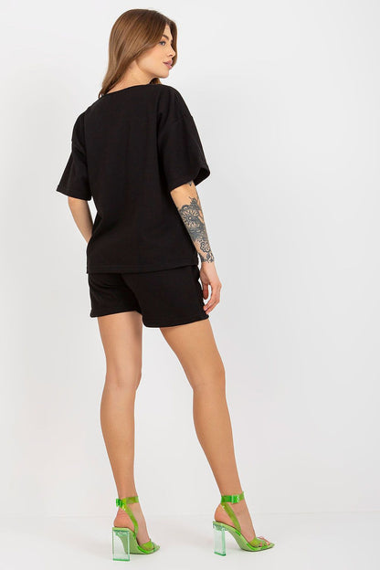 Back view of Ex Moda's luxurious cotton tracksuit set, highlighting the elegant black design, shorts with waist tie, and pairing with striking green heels.