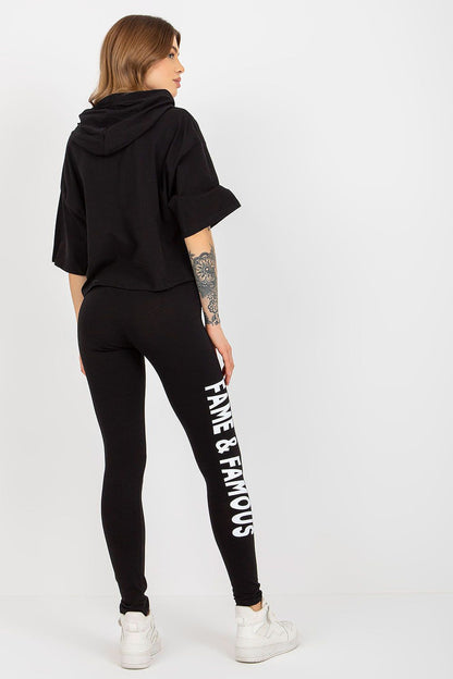 Back view of Ex Moda's elegant women's cotton sweatshirt and leggings set, showcasing the black hoodie with the inscription 'FAME' and fitted black leggings with 'FAME & FAMOUS' along the side.