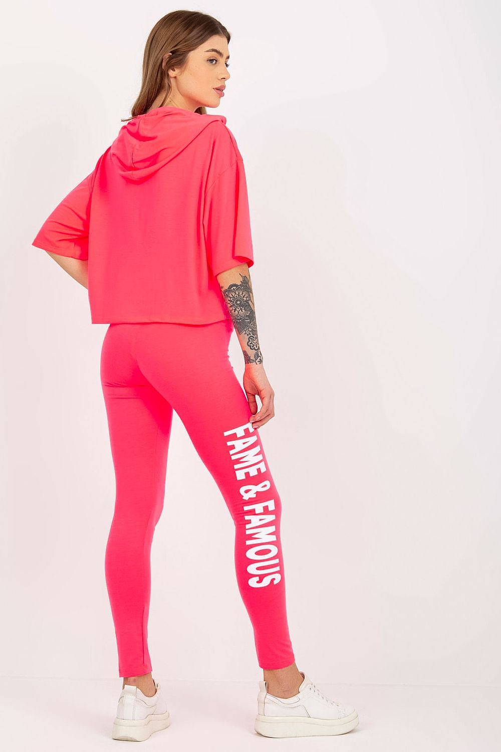 Back view of a model wearing Ex Moda's striking pink cotton sweatshirt and leggings set, featuring a cropped hoodie and fitted leggings with 'FAME & FAMOUS' text, perfect for a modern casual look.