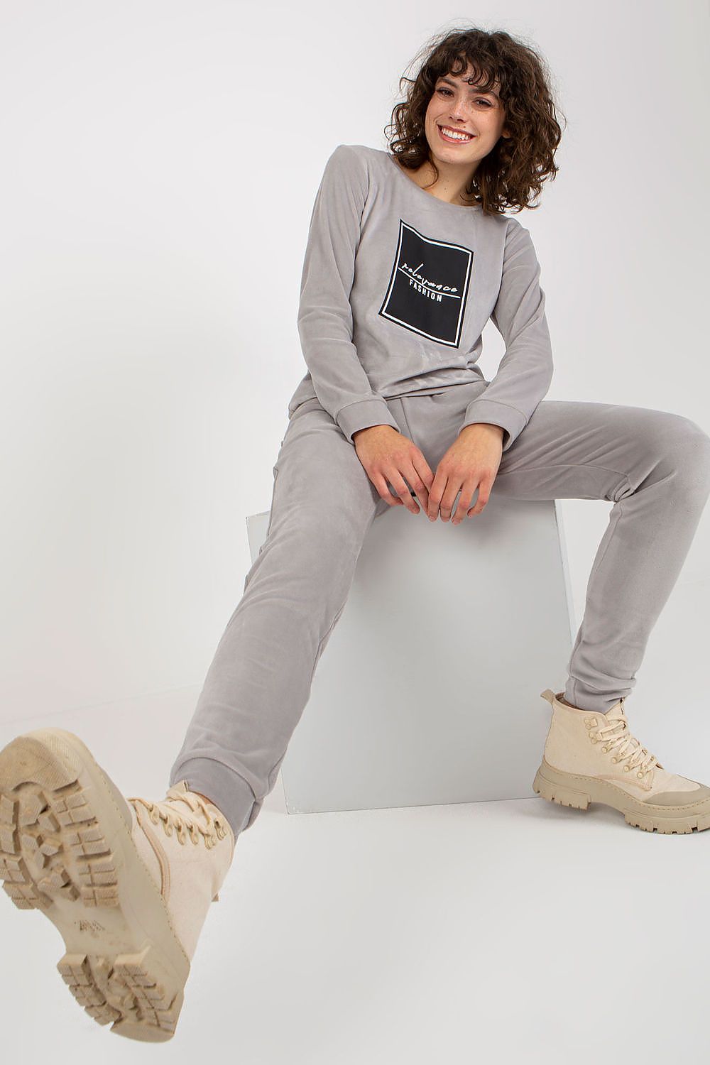 Chic and elegant grey velour tracksuit by Relevance, showcasing a model seated in a relaxed pose, wearing a sweatshirt and pants, ideal for casual sophistication.