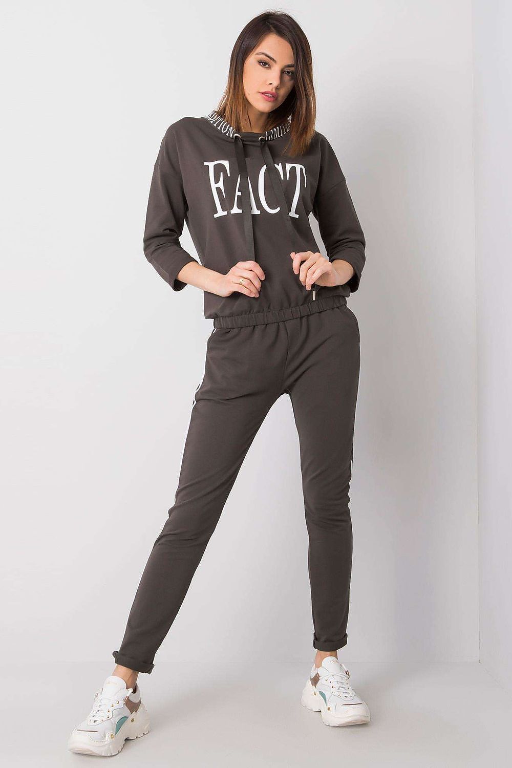 A stylish woman modelling the Elegant Women's 2-Piece Tracksuit Set by Relevance, featuring a chic 3/4 sleeve sweatshirt with a bold 'FACT' print and tailored long pants, perfect for a sophisticated athleisure look.