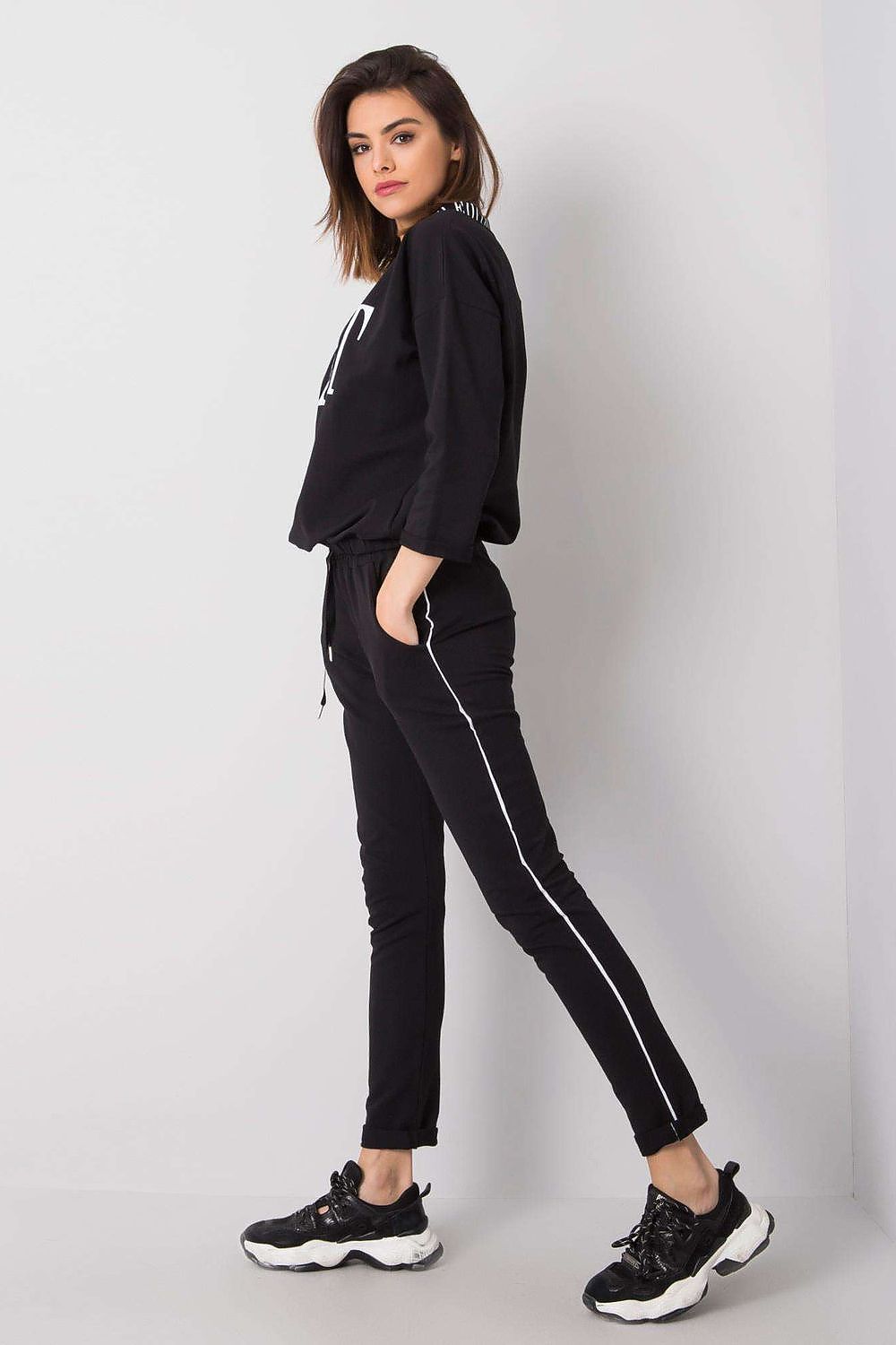 Side angle of a stylish women's black tracksuit with an emphasis on the sporty design, including a 3/4 sleeve top and streamlined pants, from Relevance.