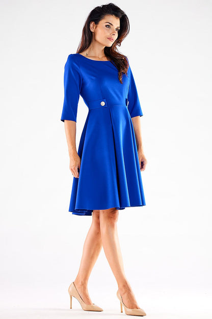 Elegant woman wearing a vibrant blue Blushed Awama daydress, showcasing a flattering silhouette with decorative buttons and short sleeves, styled with nude heels.