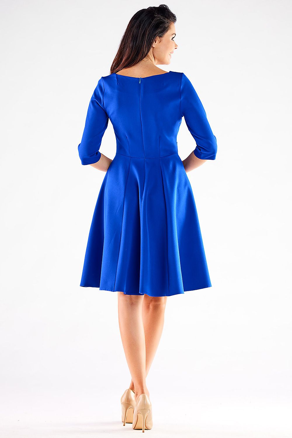Rear view of an elegant woman in a blue Blushed Awama daydress, featuring a flared skirt and short sleeves, with subtle button detailing, complemented by nude footwear.