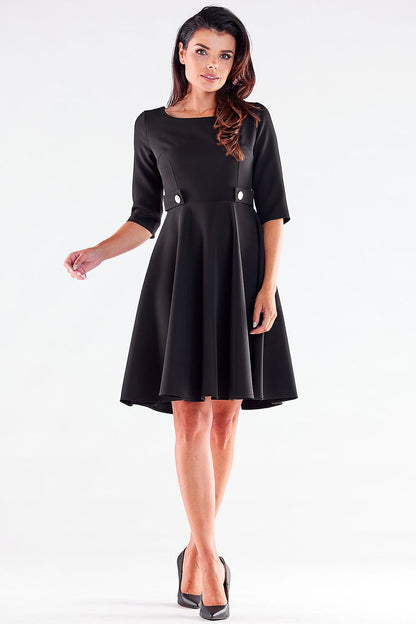 Front view of a graceful woman in a black Blushed Awama daydress, featuring stylish button accents and flowing skirt, paired with classic black heels.