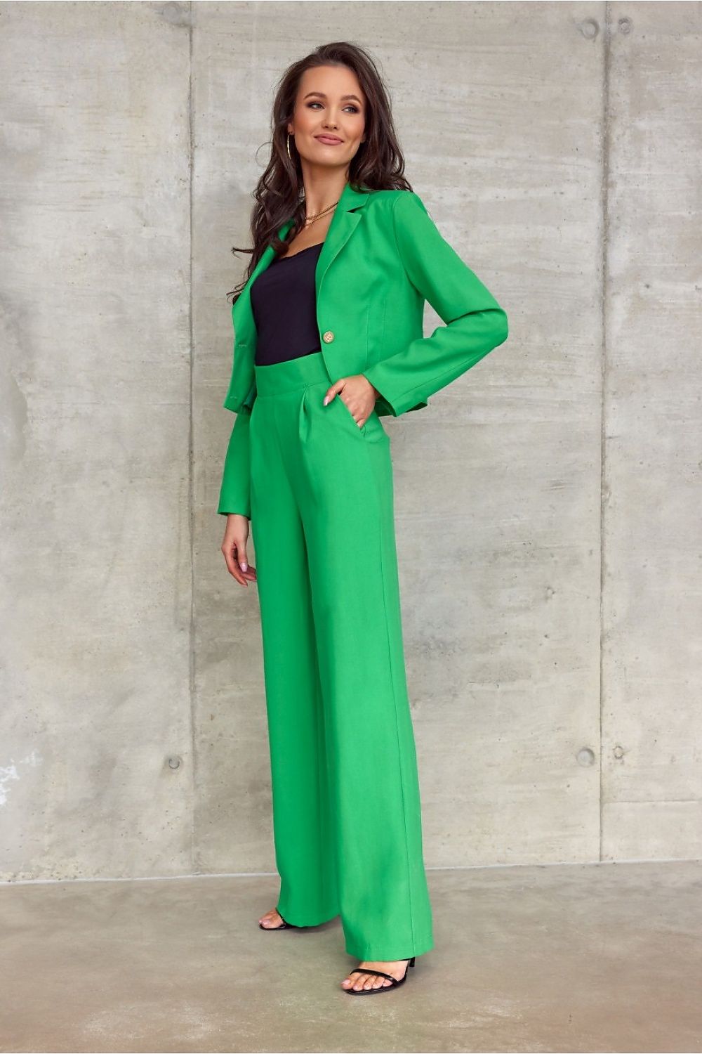 Sophisticated view of high-waisted bell-bottom trousers from Roco Fashion, highlighted in striking green, complemented by a chic black top, embodying luxury style in a modern setting.
