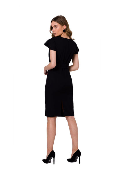Stylove black cocktail dress with a decorative fabric layer and buckled belt, model displaying the back view with a stylish slit.