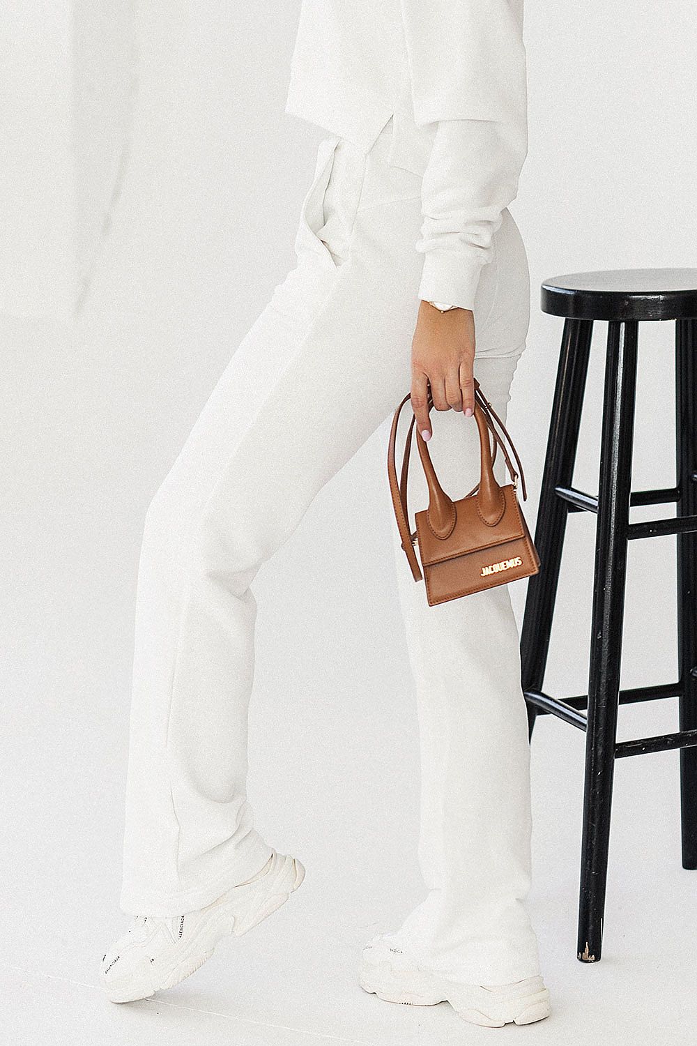 Fashionable woman holding a brown handbag while wearing IVON cotton blend sweatpants. The ensemble features slip pockets and an elastic waistband, embodying a blend of comfort and elegant style.