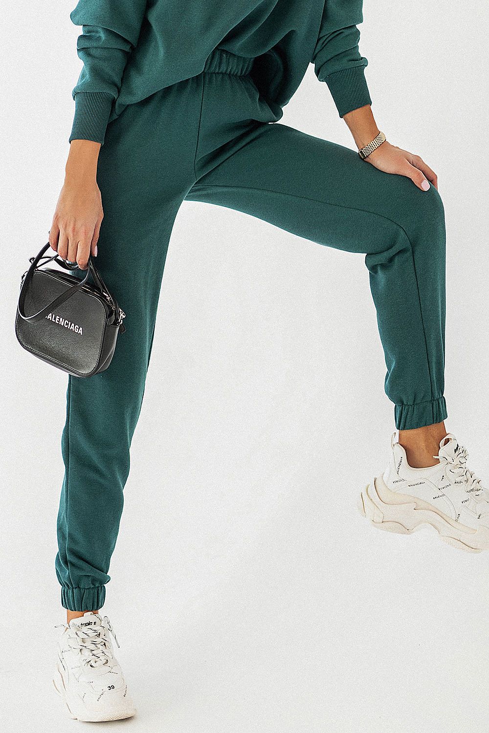 Chic IVON joggers in rich dark green fabric with elastic cuffs, paired with contemporary white sneakers and a fashionable black handbag.