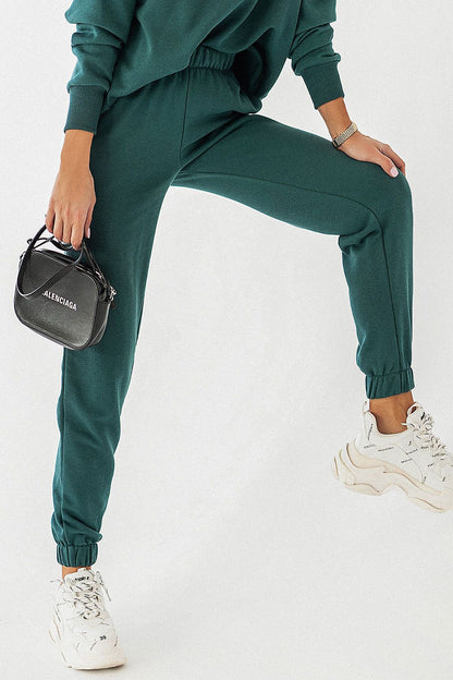 Chic IVON joggers in rich dark green fabric with elastic cuffs, paired with contemporary white sneakers and a fashionable black handbag.
