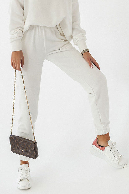 Woman wearing luxury cotton blend joggers IVON in white, paired with a matching sweatshirt and white sneakers, showcasing a chic and comfortable outfit for casual occasions.