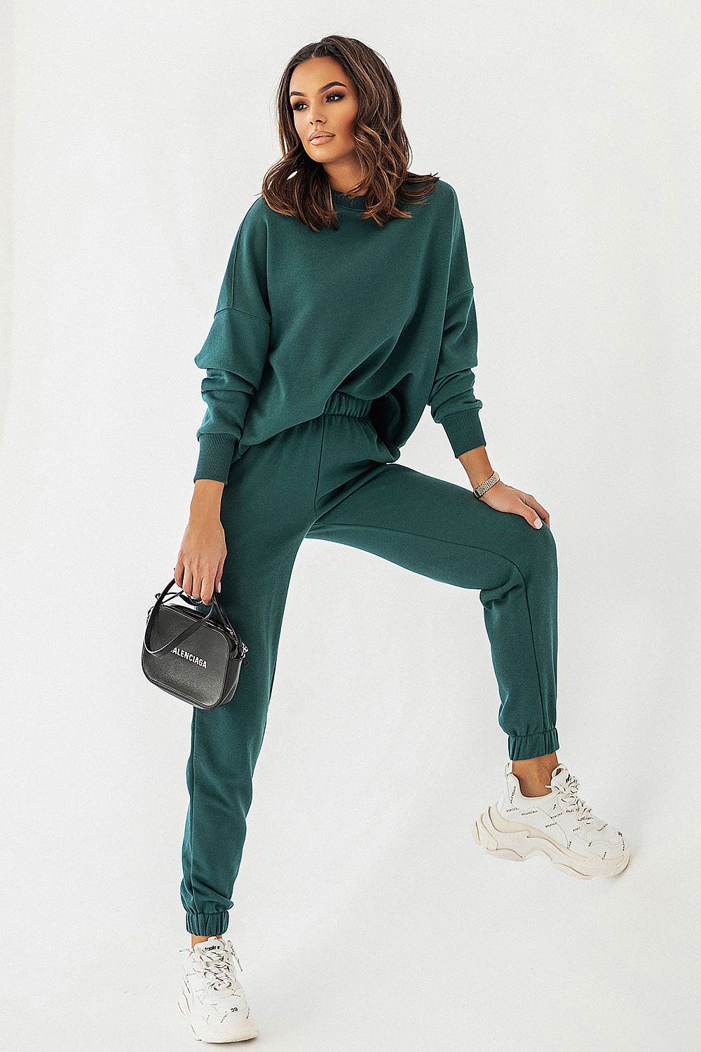 Fashionable woman showcasing the IVON oversized sweatshirt set in a rich green hue, paired with stylish joggers and a chic black handbag, epitomising casual elegance.