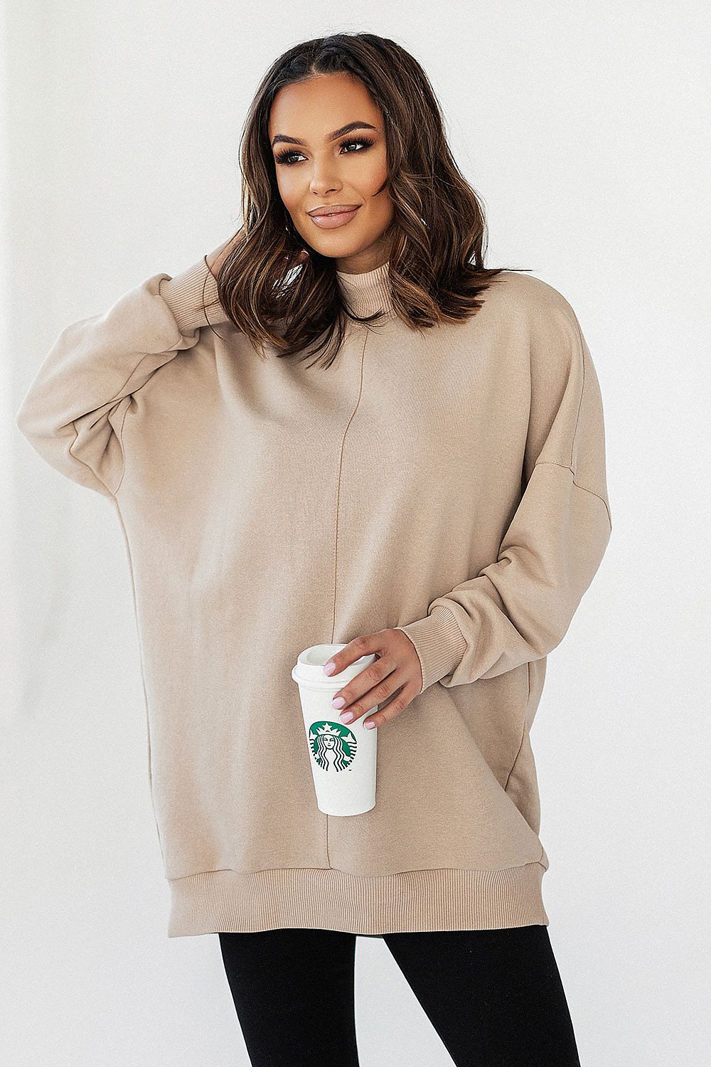 Model presenting the Luxury IVON Extended Cut Sweatshirt in beige, holding a coffee cup, styled with slim black leggings.