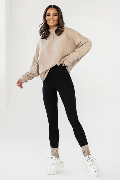 Joyful model in the Luxury IVON Extended Cut Sweatshirt in beige, paired with high-waisted black leggings and white sneakers.