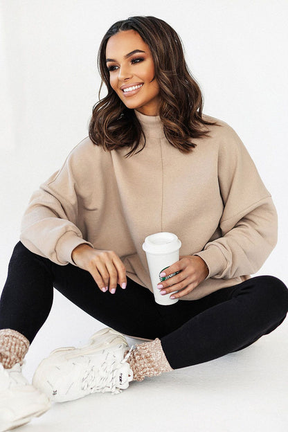 Luxurious IVON Extended Cut Sweatshirt in soft beige cotton, featuring a low collar, showcased by a stylish model sipping coffee, sitting gracefully in a relaxed pose.