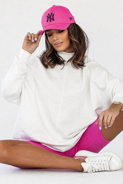 Chic fashion statement featuring a model sitting in the Luxury IVON Extended Cut Sweatshirt, complemented by pink shorts and a matching cap, exuding casual luxury.