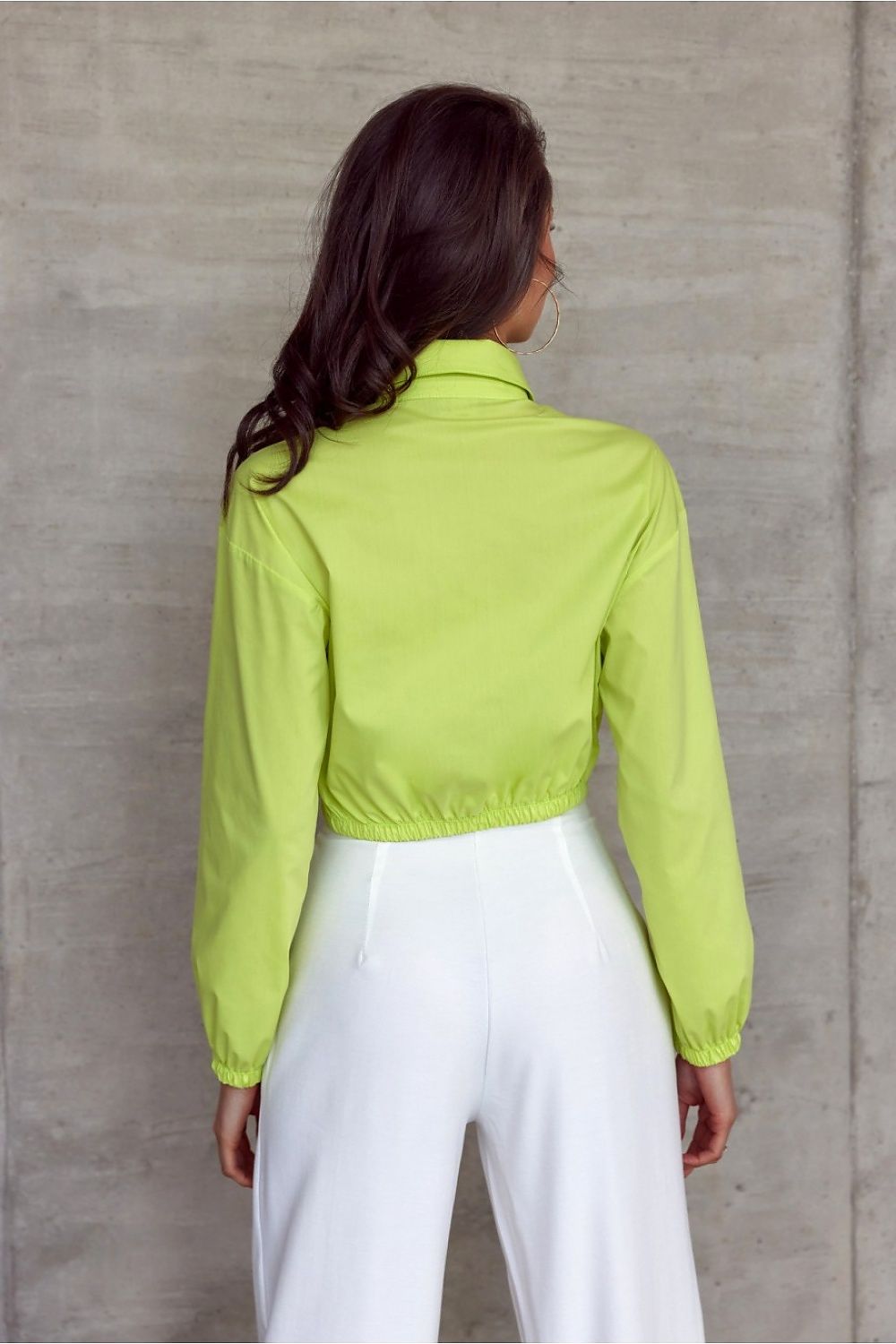 Sophisticated back view of the Roco Fashion long sleeve shirt in luminous lime green, designed with a flattering fit and ribbed accents, worn with classic white pants against a minimalist backdrop.