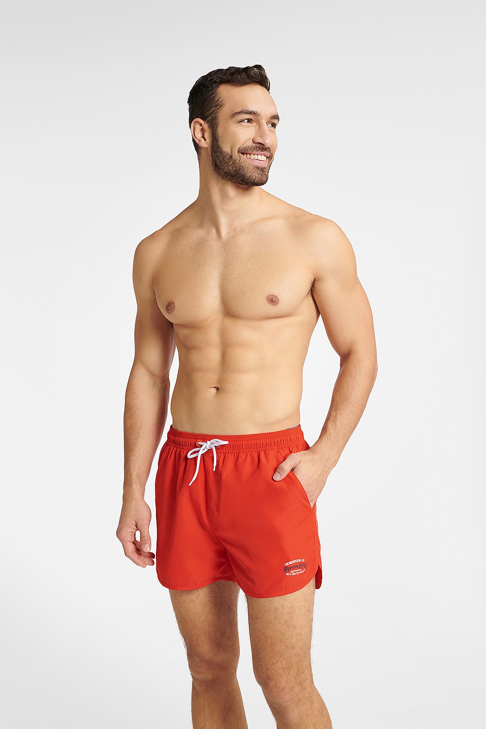 Henderson Men's quick-drying swim trunks in classic red, featuring an adjustable waist and sleek design, model showcasing the front view with a confident smile on a light background.
