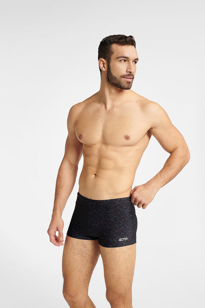 Stylish Henderson men's black swim trunks designed in a classic boxer style, featuring a sophisticated grey-red pattern, showcased on a fit model in an elegant pose for a luxurious beachwear look.