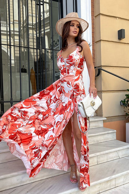 Elegant woman in a floral satin long dress with a slit, accessorised with a stylish hat and handbag, showcasing Bicotone's luxurious fashion on a marble staircase.