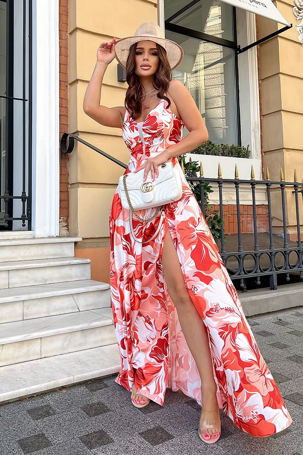 Sophisticated floral satin long dress with slit and fitted waist by Bicotone, model posing gracefully with a hat and designer handbag on a picturesque staircase.