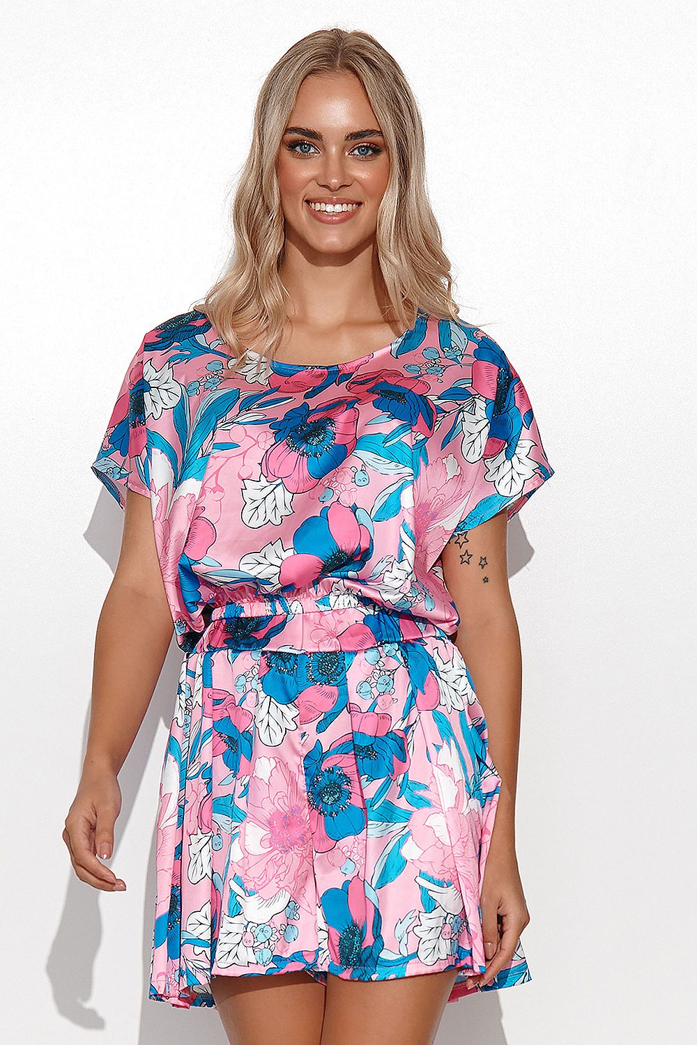 Elegant woman wearing a vibrant floral satin summer set featuring a short blouse and high-waisted shorts by Makadamia, showcasing her stylish look against a light background.