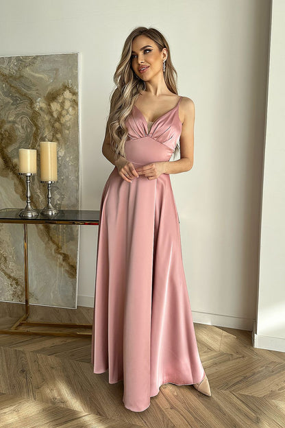 Elegant satin evening dress by Bicotone, featuring a stylish cut-out top and flowy skirt, model showcasing the soft pink hue in a chic indoor setting.