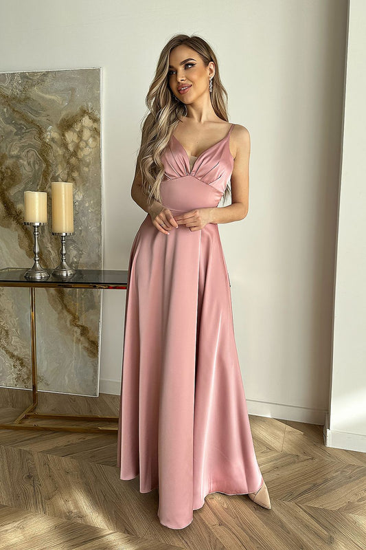 Elegant satin evening dress by Bicotone, featuring a stylish cut-out top and flowy skirt, model showcasing the soft pink hue in a chic indoor setting.