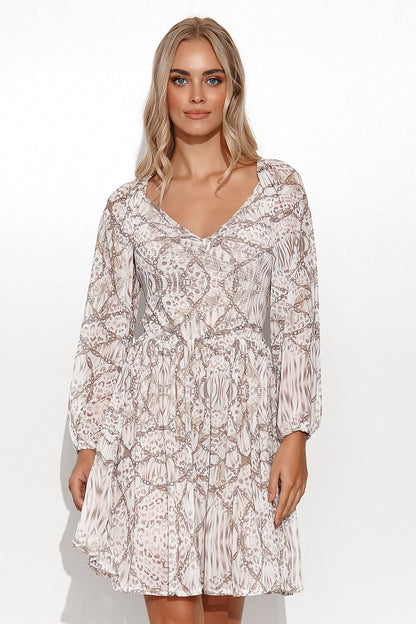 Elegant Makadamia Airy Daydress featuring a girly cut and long sleeves, complemented by a bow detail. Model showcases the dress in a luxurious patterned mesh with a high-cut neckline.