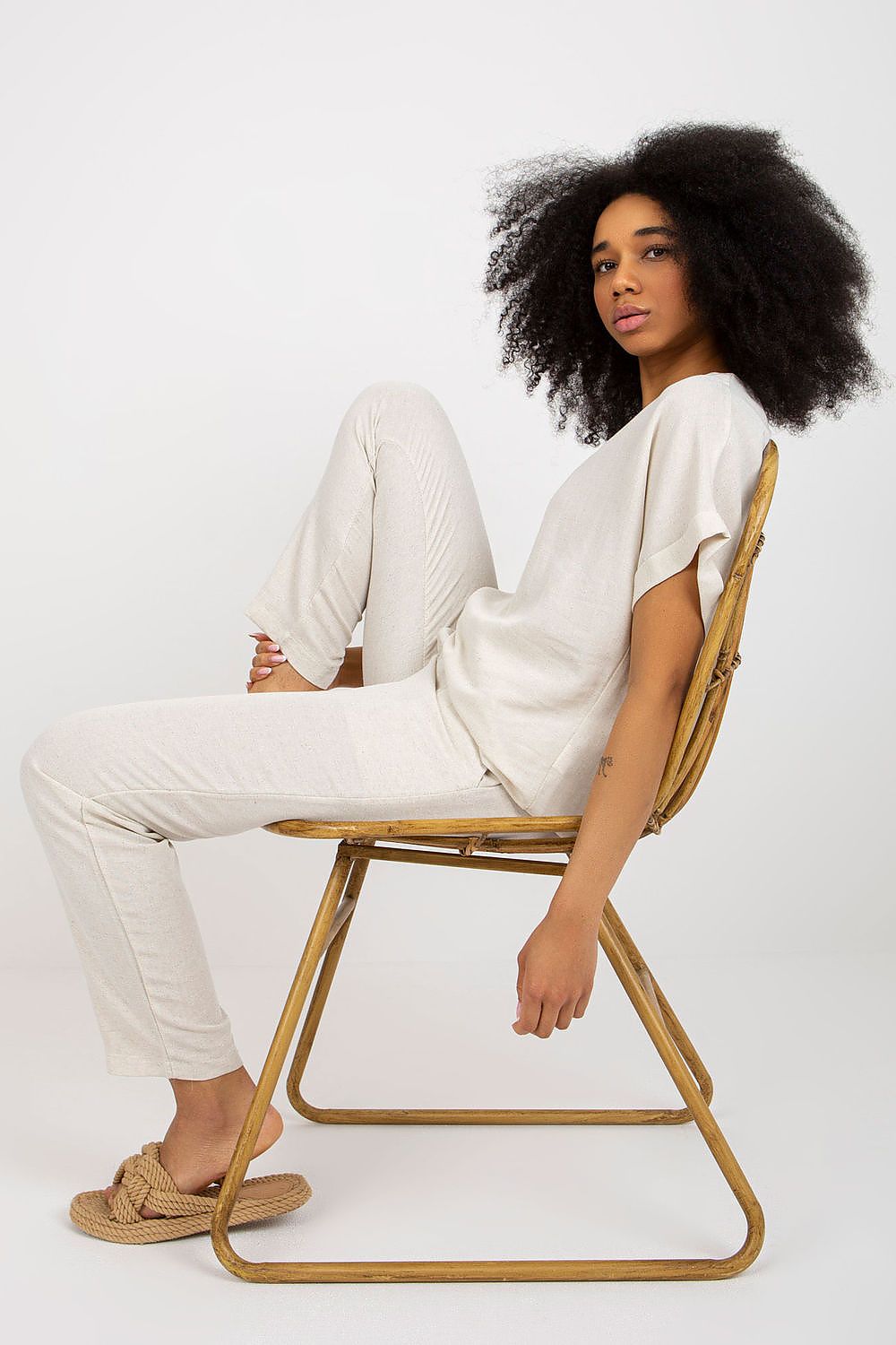 Sophisticated style of the Rue Paris summer set presented by a model sitting elegantly on a chair, highlighting the relaxed fit of the blouse and tailored trousers.