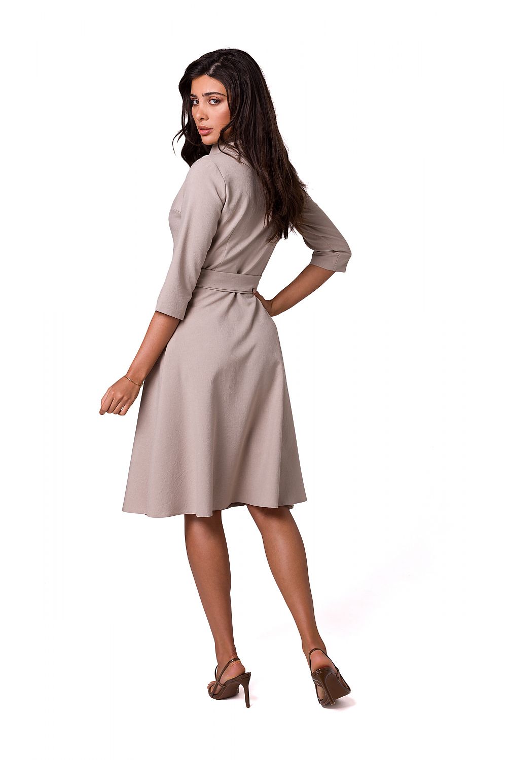 Back view of a luxurious flared daydress by BeWear, showcasing a shawl collar and tied waist, model displaying the sophisticated design in a soft beige hue.