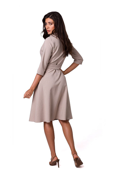 Back view of a luxurious flared daydress by BeWear, showcasing a shawl collar and tied waist, model displaying the sophisticated design in a soft beige hue.