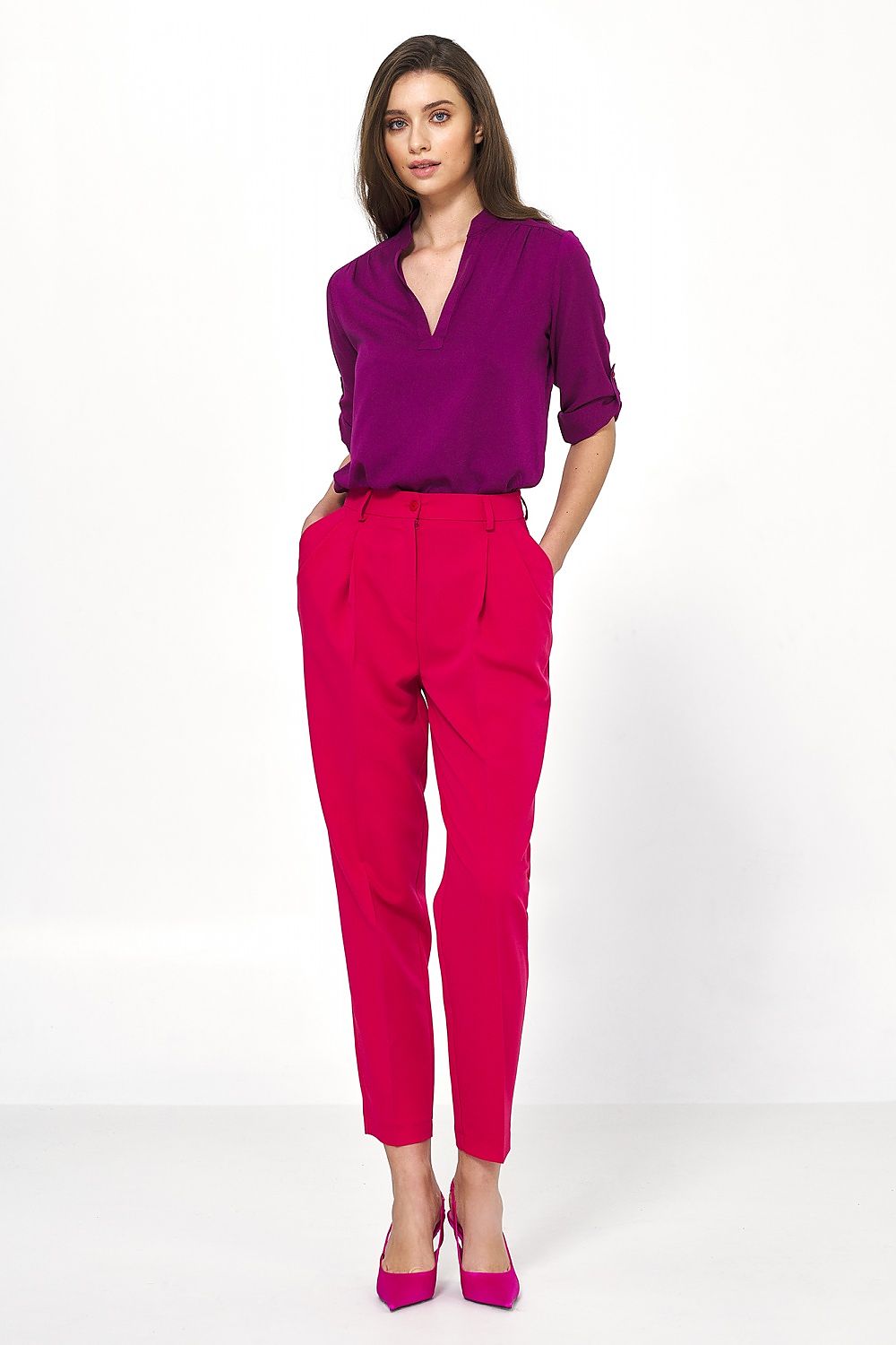 Elegant woman wearing high-waisted balloon trousers in vibrant pink by Nife, paired with a stylish purple blouse and pink heels, showcasing a chic office-ready look.