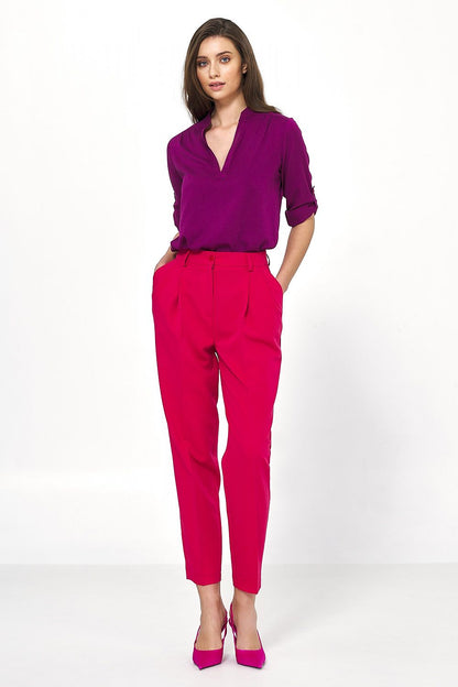 Elegant woman wearing high-waisted balloon trousers in vibrant pink by Nife, paired with a stylish purple blouse and pink heels, showcasing a chic office-ready look.