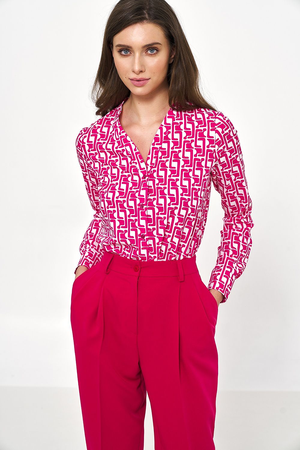 Chic model showcasing an elegant long sleeve button-down shirt by Nife, featuring a striking pink geometric pattern, paired with tailored high-waisted trousers for a sophisticated office look.