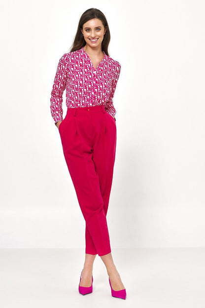 Stylish woman smiling while wearing an elegant long sleeve button-down shirt by Nife with a vibrant pink geometric design, complemented by tailored pink trousers, perfect for a luxury office ensemble.